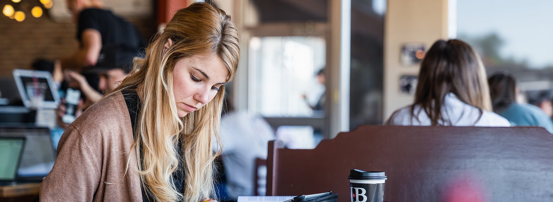 Student in a Coffee Shop Girl reading through a book taking notes at table in a coffee shop